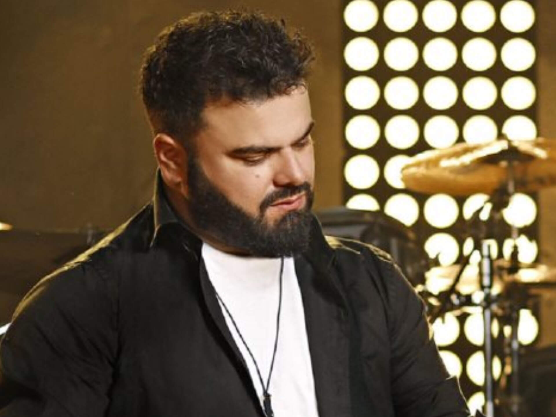 Ο Ηλίας Καμπακάκης, φορώντας μαύρο πουκάμισο τραγουδά σε μικρόφωνο στη σκηνή